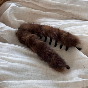 Gros plan sur la barrette banane en fausse fourrure marron sur tissu beige doux