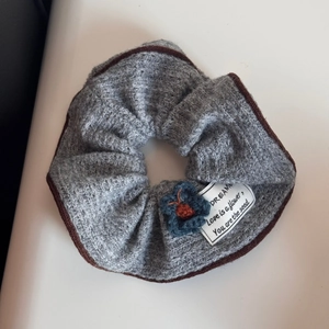 Detail of grey knitted hair scrunchie with leopard edge and embroidered text label