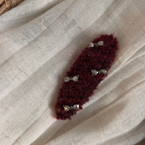 Close-up of burgundy knit hair clip with sparkling rhinestone bows on soft fabric