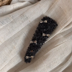 Close-up of plush dark gray hair clip with four sparkling rhinestone bow decorations