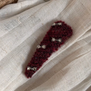 Close-up of a burgundy knitted hair clip featuring four silver rhinestone bow accents