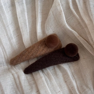 Detailed texture of knitted brown BB hair clips with velvet ball accents on fabric