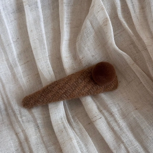 Close-up of brown knitted triangle hair clip with soft plush pom pom on linen background