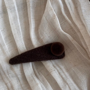 Close-up of retro dark brown flocked BB hair clip with plush ball on soft fabric background