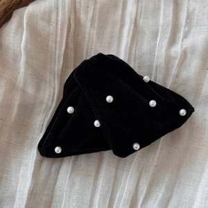 Close-up of black velvet hair clip with white faux pearls on soft beige linen fabric