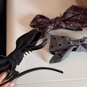 Close-up of three bow hair clips in solid black, plaid, and heart patterns with matte finish