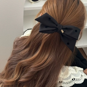 Detail of a large black bow hair clip with polka dots on elegant wavy brown hair
