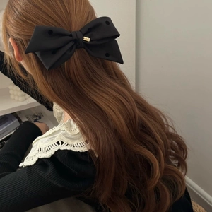 Detailed view of a large black satin bow hair clip with a golden metal tag on wavy hair