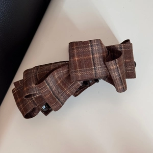 Detailed macro view of brown checkered fabric bow clip with black plastic comb teeth