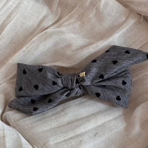Detail of grey bow hair clip with black heart pattern and gold metal square buckle
