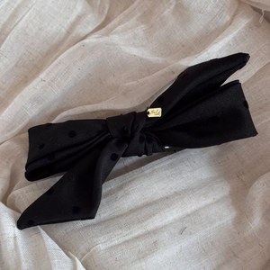 Detail of black polka dot bow hair clip with gold Hand made metal tag on linen