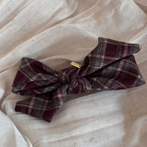 Detailed close-up of a burgundy plaid bow hair clip with an elegant gold metal accent