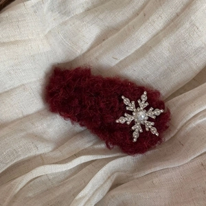 Close-up of plush burgundy hair clip with silver rhinestone snowflake and pearl detail
