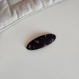 Detailaufnahme einer ovalen Filz-Haarklammer mit weiß gestickten Schleifenmustern