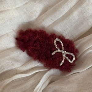 Close-up of plush wine red floral hair clip with silver rhinestone bow on linen background