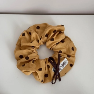 Détail du chouchou jaune à pois avec nœud en cuir marron et étiquette en tissu