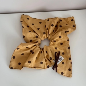 Gros plan d'un chouchou jaune à pois avec nœud en soie marron et étiquette tissée