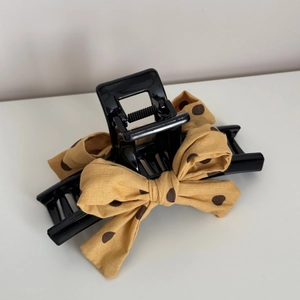 Détail d'une pince à cheveux noire avec un nœud en tissu jaune gingembre à pois
