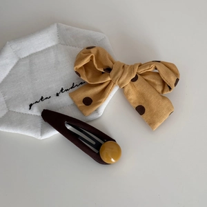 Détail d'un nœud papillon jaune à pois et d'une barrette marron avec perle jaune