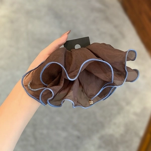 Brown mesh scrunchie with blue edges and a gold bell pendant shown in a hand-held view