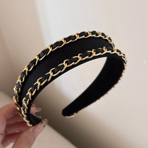 Close-up of black leather headband featuring dual golden metal chain details and woven fabric