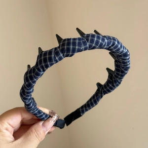 Detail of blue plaid headband with black decorative spikes and soft fabric end caps