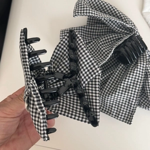 Detail view of black and white plaid bow hair claw clip being held to show mechanism