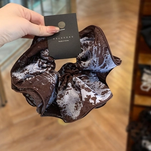 Close-up of silk scrunchie with marble tie-dye pattern in brown and lilac colors