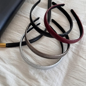 Flat lay of thin PU leather headbands in black, burgundy and silver on white fabric
