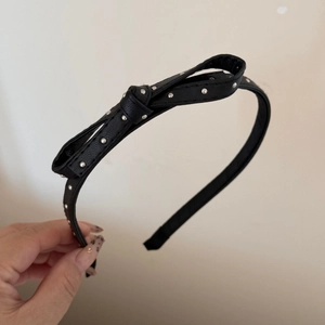 Detail of black faux leather headband with silver metal rivets and a bow knot accessory