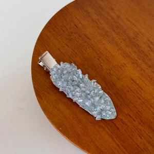 Macro detail of leaf-shaped duckbill hair clip with blue rhinestones on wooden tray