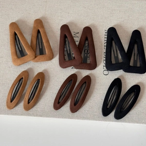 Détail de pinces à cheveux en velours marron et noir sur un tissu texturé beige