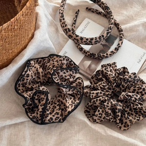 Flat lay of leopard print hair scrunchies and headbands on textured beige fabric