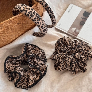 Detail view of leopard print hair scrunchies and headbands on natural beige linen background