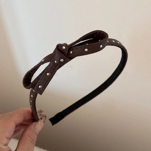 Detail of a dark brown leather headband featuring a 3D bow and silver polka dot studs