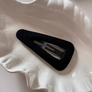 Gros plan sur une pince à cheveux triangle noire floquée sur un plateau blanc