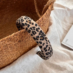 Close-up of a wide leopard print headband resting on a woven basket with beige linen