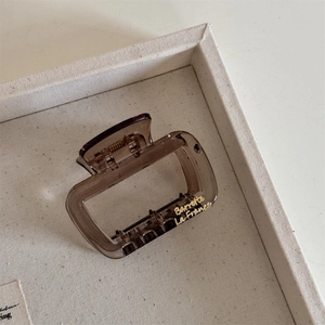 Detail view of a translucent brown square hair claw clip with gold lettering on canvas