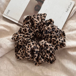 Detailed view of leopard print oversized scrunchie on beige linen fabric texture