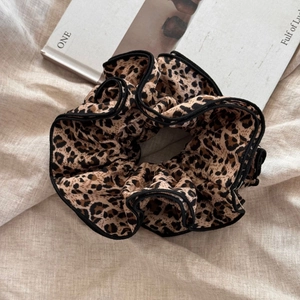 Detail of oversized leopard print hair scrunchie with black ruffled edges on linen fabric