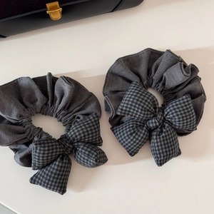 Détail de deux chouchous à nœud à carreaux gris sur un fond clair minimaliste
