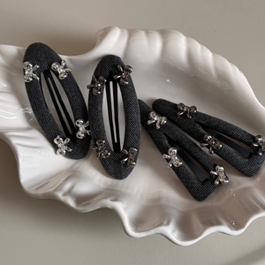 Detail of four dark grey textured fabric hair clips with silver metal bows on a ceramic tray