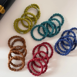 Dettaglio di 25 elastici per capelli a costine colorati in toni oliva, blu, marrone e rosso