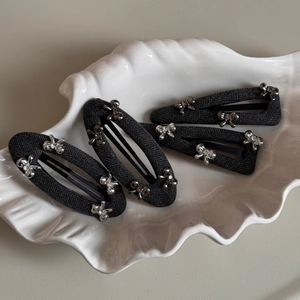 Set of four grey twill bow hair clips with silver rhinestones on a white shell tray
