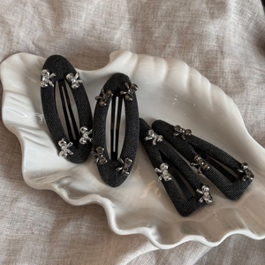 Detail of four black woven BB hair clips with silver flower accents in a white shell dish