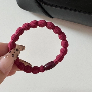 Dettaglio dell'elastico per capelli bordeaux testurizzato con elegante perla in resina lucida