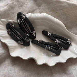 Detail of four grey textured hair clips with silver metal bows in a white shell dish