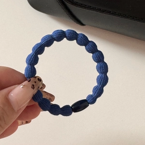 Dettaglio dell'elastico per capelli blu scuro a bolle con fibbia nera tenuto in mano