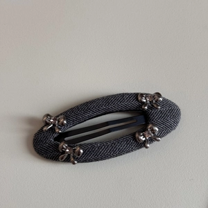 Detail of grey herringbone fabric hair clip with four silver metal bows and tiny rhinestones
