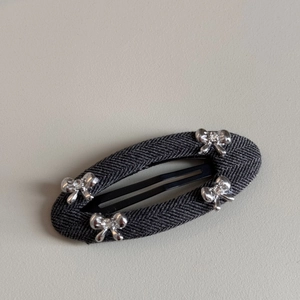 Detail of grey herringbone fabric oval hair clip with four silver metal bows